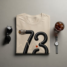 Load image into Gallery viewer, Cream t-shirt with black cord forming the number 73 and wave graphic.