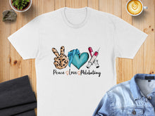 Load image into Gallery viewer, White t-shirt with "Peace Love Phlebotomy" graphic, featuring peace sign, heart, and syringes.