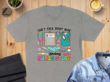 Load image into Gallery viewer, Gray t-shirt with "CAN'T TALK RIGHT NOW DOING NURSE STUFF" text and medical icons.