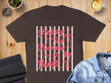 Load image into Gallery viewer, Brown t-shirt with pink text "Helping Tiny Humans Do Big Things" and ribbons.