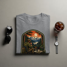 Load image into Gallery viewer, T-shirt graphic of a man using a radio in a mountain landscape at sunset.