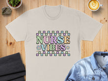 Load image into Gallery viewer, Cream t-shirt with "Nurse Vibes" in pastel checkered text and floral accents.