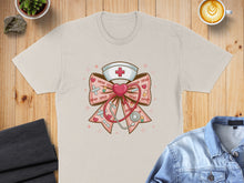 Load image into Gallery viewer, Cream t-shirt with a pastel nurse's cap and stethoscope adorned with pink bows and "xoxo."