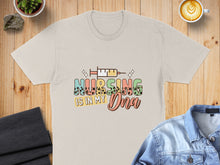 Load image into Gallery viewer, T-shirt with colorful text "Nursing is in my DNA" and syringe graphic.