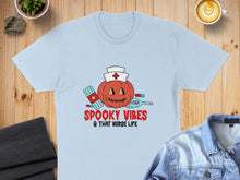 Load image into Gallery viewer, Light blue t-shirt with a Halloween pumpkin, bandages, and thermometer, reading "Spooky Vibes & That Nurse Life."