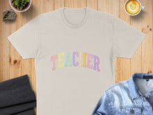 Load image into Gallery viewer, Beige t-shirt with pastel "TEACHER" text, laid flat with coffee and denim jacket.