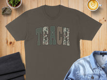 Load image into Gallery viewer, Brown t-shirt with "TEACH" in camouflage font, surrounded by coffee and denim jacket.