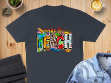Load image into Gallery viewer, "Made to Teach" graphic on charcoal t-shirt with school supply accents.