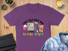 Load image into Gallery viewer, Purple t-shirt with "Can't talk right now, doing nurse stuff" text and medical icons.