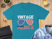 Load image into Gallery viewer, Teal t-shirt with "Vintage America" text and American flag sunglasses.