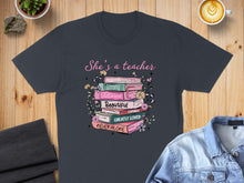 Load image into Gallery viewer, T-shirt with stack of books featuring "She's a teacher" and Bible verse.