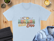 Load image into Gallery viewer, Light blue t-shirt with "Nursing Is In My DNA" text and syringe graphic.
