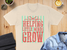 Load image into Gallery viewer, Cream t-shirt with "Helping Little Minds Grow" text in red and green stripes.
