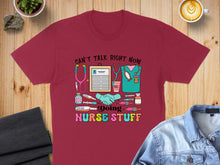 Load image into Gallery viewer, Burgundy t-shirt with "Can't talk right now, doing nurse stuff" text and medical graphics.
