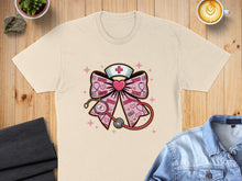 Load image into Gallery viewer, Pink bow with stethoscope, heart, and XOXO pattern on a cream t-shirt.
