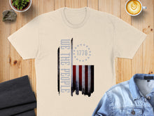 Load image into Gallery viewer, Cream t-shirt with distressed American flag graphic and "WE THE PEOPLE" text.
