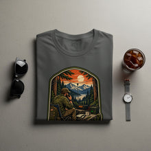 Load image into Gallery viewer, T-shirt graphic of man using ham radio in a mountain landscape at sunset.
