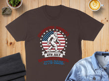 Load image into Gallery viewer, T-shirt with Bigfoot, US flag, and text "Celebrating America's 4th of July Semiquincentennial 1776-2026".
