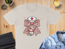Load image into Gallery viewer, Cream t-shirt with a pink bow featuring a stethoscope, nurse's hat, and "XOXO" text.
