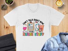 Load image into Gallery viewer, White t-shirt with "CAN'T TALK RIGHT NOW DOING NURSE STUFF" and medical icons.
