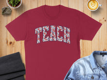 Load image into Gallery viewer, Maroon t-shirt with "TEACH" in red, white, and blue floral lettering.
