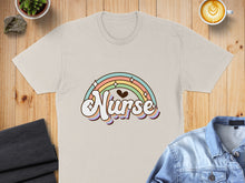 Load image into Gallery viewer, Beige t-shirt with "Nurse" in a rainbow arch, set against a wooden surface.
