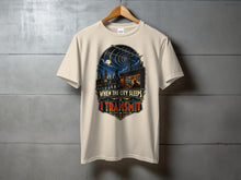 Load image into Gallery viewer, Cream t-shirt with graphic depicting a city skyline at night and text "When the city sleeps, I transmit".
