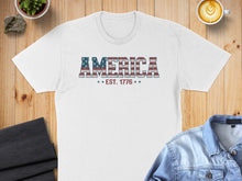 Load image into Gallery viewer, White t-shirt with "AMERICA EST. 1776" text in distressed flag design.
