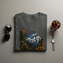Load image into Gallery viewer, T-shirt with a graphic of a man using a radio in a mountainous forest setting.
