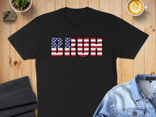 Load image into Gallery viewer, Black t-shirt with "BRUH" in American flag letters, on wooden surface.
