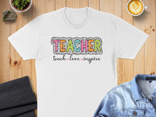 Load image into Gallery viewer, White t-shirt with colorful "TEACHER" text and "teach love inspire" slogan.
