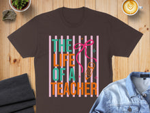 Load image into Gallery viewer, Brown t-shirt with colorful "The Life of a Teacher" text and pink bow.

