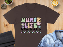 Load image into Gallery viewer, Brown t-shirt with "Nurse Life Is The Best Life" text in pastel colors.
