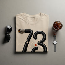 Load image into Gallery viewer, Cream t-shirt with black hose forming the number 73, a wavy line, and an orange dot.
