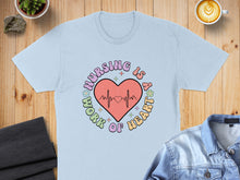 Load image into Gallery viewer, Light blue t-shirt with "Nursing is a work of heart" circular graphic.
