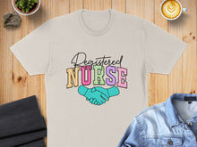 Load image into Gallery viewer, Registered Nurse text with shaking hands graphic on a light tan t-shirt.
