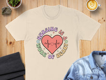 Load image into Gallery viewer, Beige t-shirt with "Nursing is a work of heart" text and heartbeat graphic.

