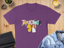 Load image into Gallery viewer, Purple t-shirt with "Teacher" text design featuring pencils, flowers, and a bow.
