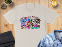 Load image into Gallery viewer, "Nurse" text design with coffee, stethoscope, and scrubs on a tan t-shirt.
