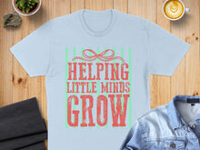 Load image into Gallery viewer, Light blue t-shirt with "Helping Little Minds Grow" text and green stripes.
