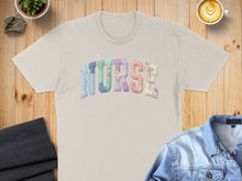 Load image into Gallery viewer, Light beige t-shirt with "NURSE" spelled out in colorful, patterned, fabric letters.
