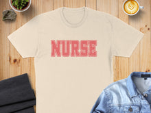 Load image into Gallery viewer, Cream t-shirt with "NURSE" in coral text, laid flat with denim jacket and coffee.
