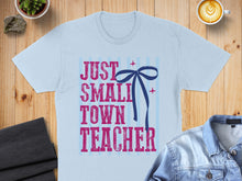 Load image into Gallery viewer, Light blue t-shirt with "JUST SMALL TOWN TEACHER" text and blue bow.
