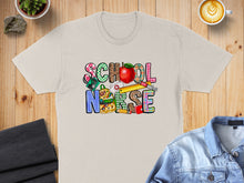 Load image into Gallery viewer, "School Nurse" text with school supplies, stethoscope, and apple graphic on a t-shirt.
