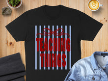 Load image into Gallery viewer, Black t-shirt with red text reading "Teaching Things" on a blue striped background.
