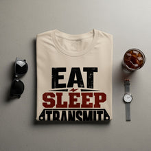Load image into Gallery viewer, Cream t-shirt with "EAT SLEEP TRANSMIT" text, sunglasses, watch, and iced coffee.
