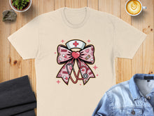 Load image into Gallery viewer, Pink bow with stethoscope, medical symbols, and XOXO patterns on a cream t-shirt.
