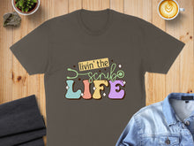 Load image into Gallery viewer, "Livin' the Scrub Life" text with stethoscope and coffee cup graphic on a dark t-shirt.
