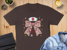 Load image into Gallery viewer, Brown t-shirt with a pink bow, stethoscope, and nurse cap graphic.
