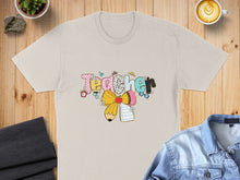 Load image into Gallery viewer, T-shirt with colorful "Teacher" text, pencil, bow, and school supplies graphic.
